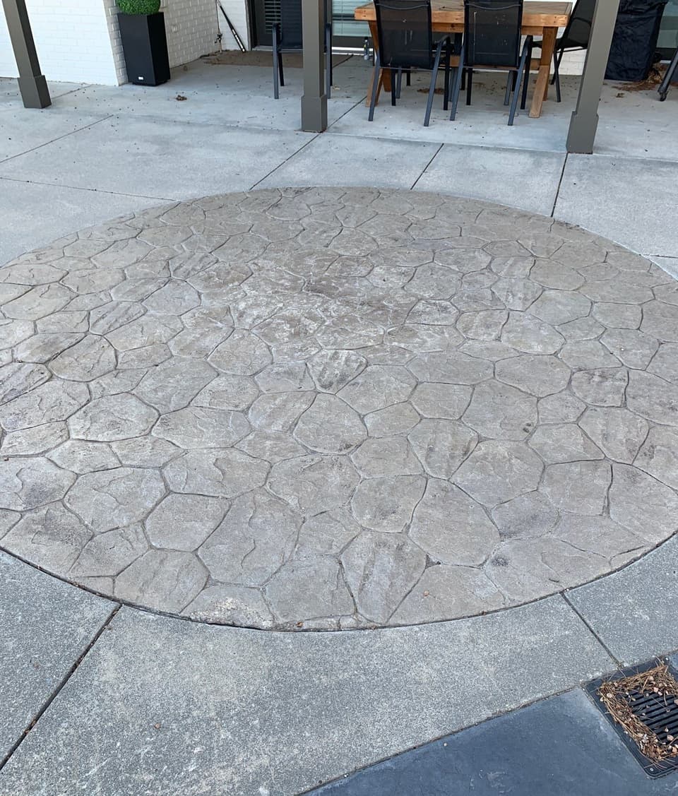 A circular decorative stamped concrete patio has been installed and finished, showing a stone-pattern design with clear detail and proper integration with surrounding concrete flatwork.