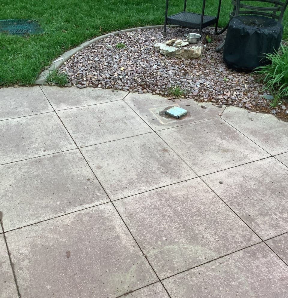 A completed concrete patio with sealed joints laid out in a grid pattern, adjacent to a gravel landscaping area and green lawn.