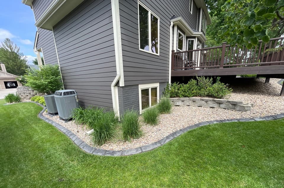A residential foundation showing an installed egress window on the basement level with completed landscaping and gravel bed edging.