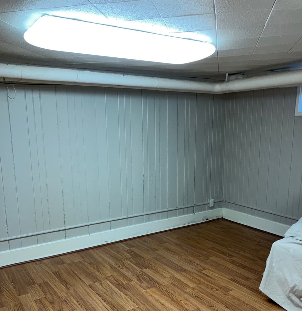 A completed crawlspace with white vapor barrier encapsulation installed on walls, finished with vinyl flooring, and new LED lighting fixture overhead.