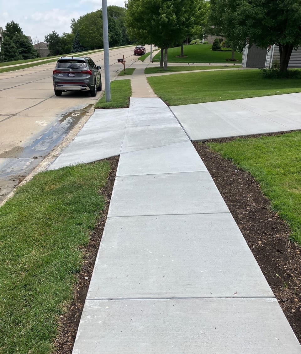 Newly installed concrete sidewalk in front of a residential property, showing clean, finished concrete flatwork with proper joints and grading.