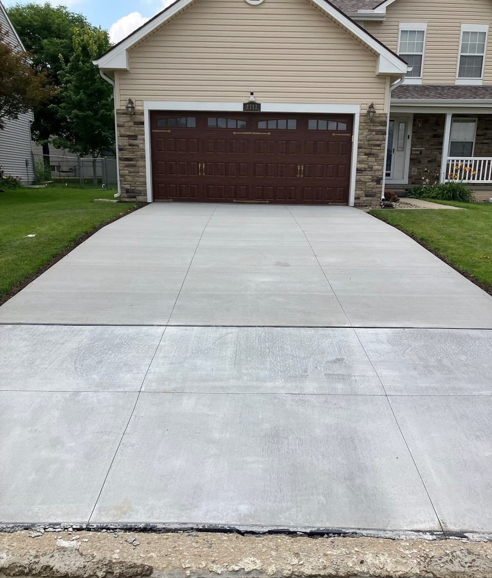 A newly poured and finished concrete driveway with control joints, showing the completed flatwork installation in front of a residential garage.