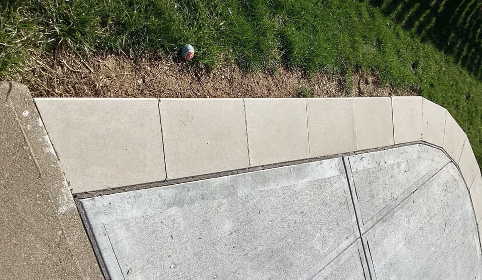 Completed concrete flatwork installation showing new concrete pad with control joints adjoining existing concrete and landscaped area above.