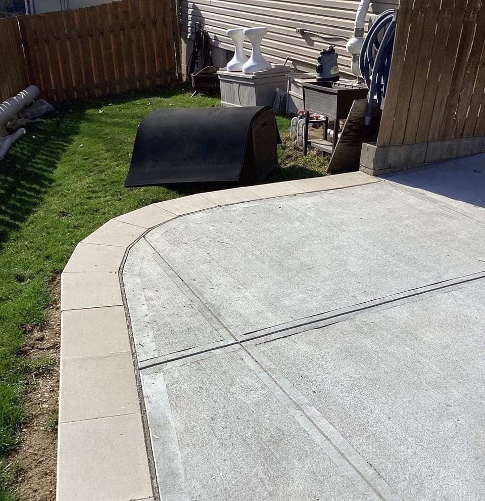 Completed concrete flatwork with control joints and sealant installed in a residential backyard, showing finished patio surface with proper grading and landscaping restored.
