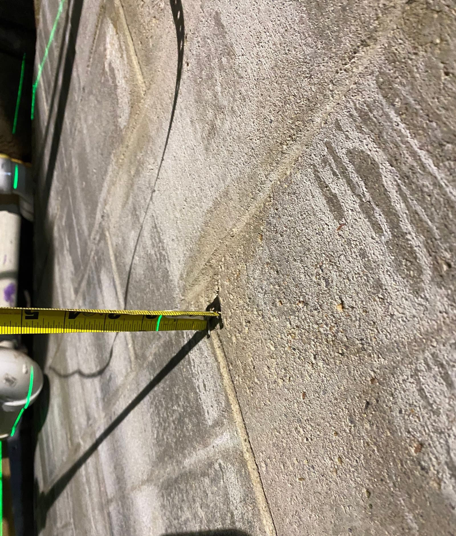 Epp Foundation Repair inspecting a cracked block foundation with a tape measure and laser level in Lincoln, NE.