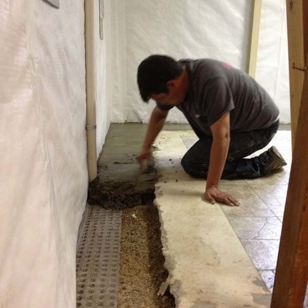 Epp Foundation Repair technician installing a crawl space drainage system and vapor barrier with concrete.