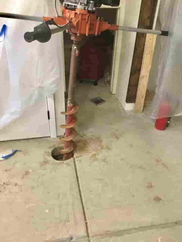Epp Foundation Repair installing helical piers with an auger drill into a concrete slab.