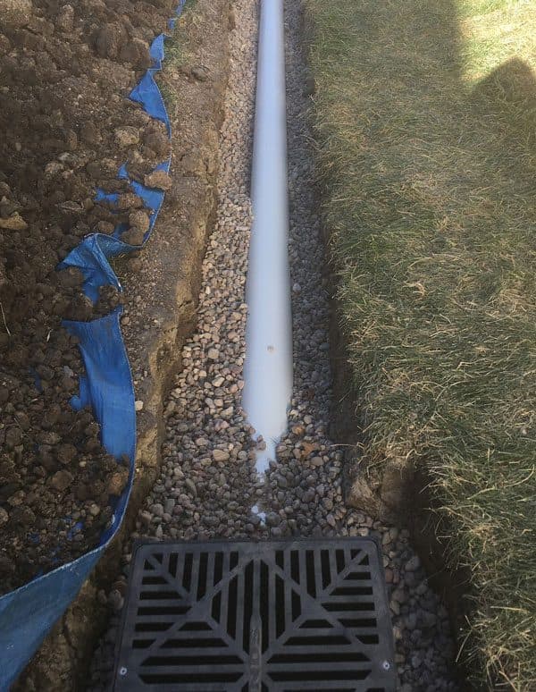 Epp Foundation Repair installing a French drain with a perforated pipe and surface drain grate in a trench.