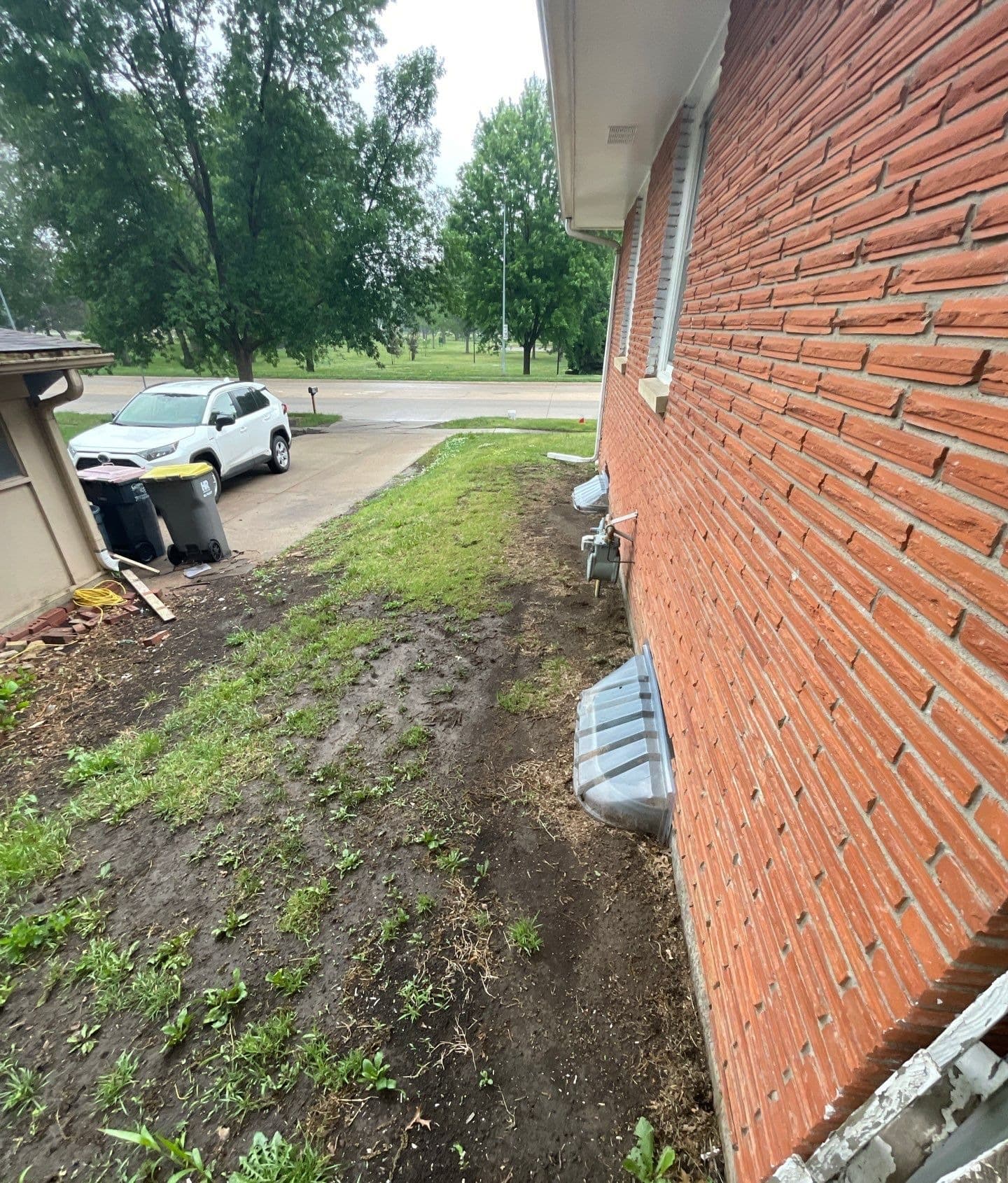 Epp Foundation Repair inspecting wet soil and poor drainage near a home's exterior foundation and window well in Lincoln, NE.