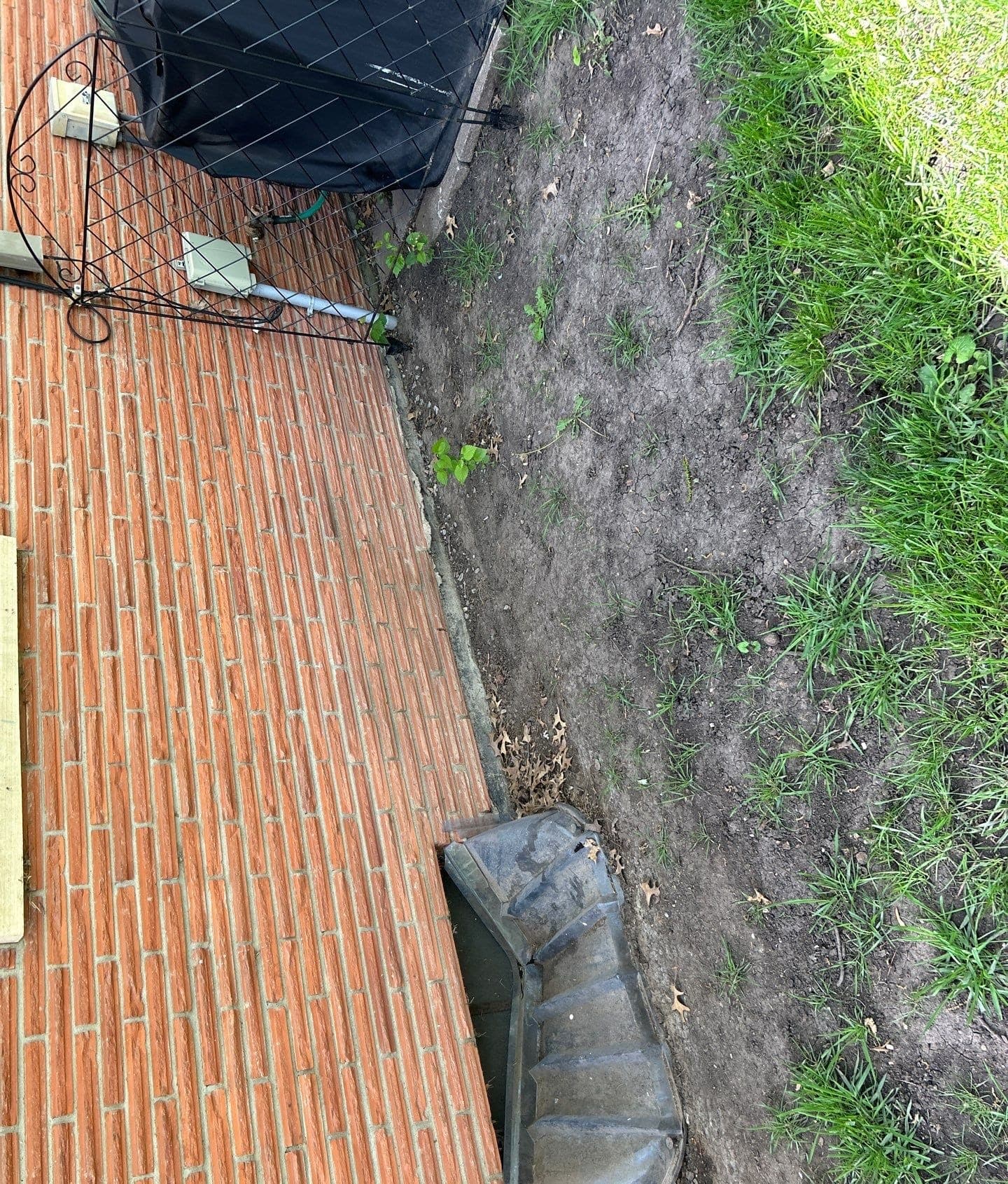 Epp Foundation Repair inspecting exterior downspout drainage with standing water near brick foundation in Lincoln, NE.
