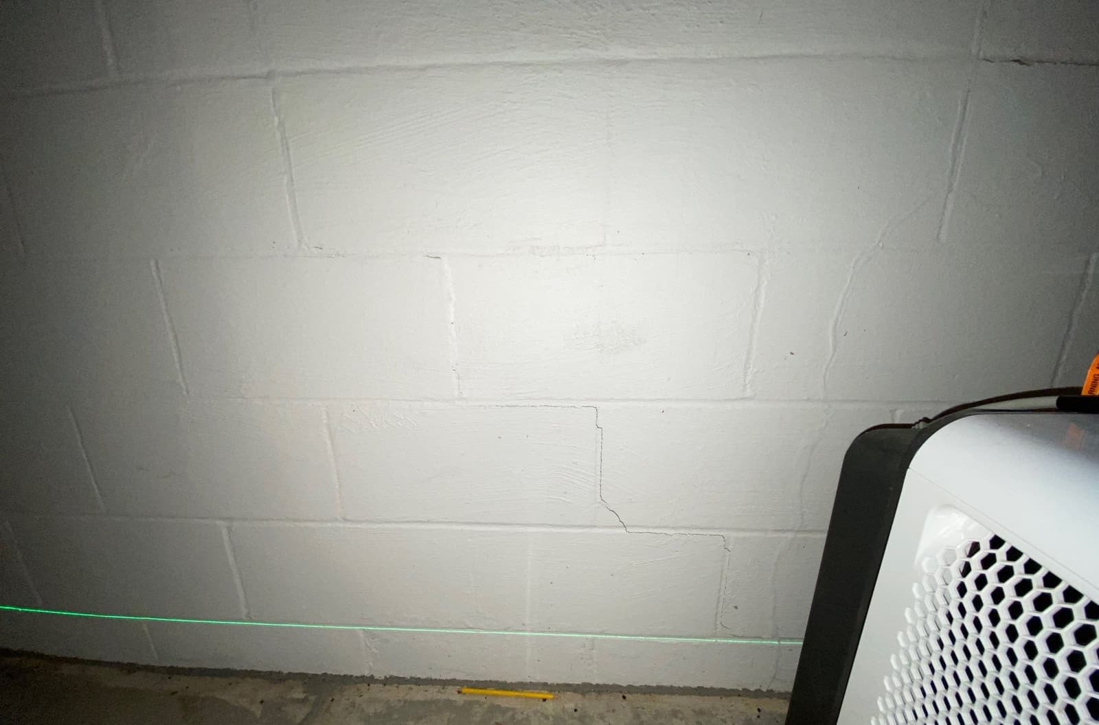 Epp Foundation Repair inspecting stair-step and horizontal cracks in a concrete block basement wall with a laser level in Lin