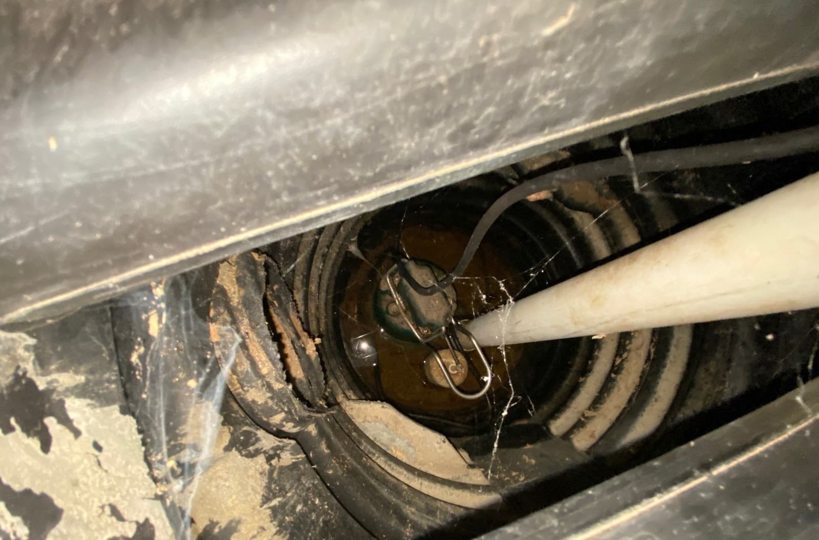 Epp Foundation Repair inspecting a dirty sump pump pit with standing water and cobwebs in Lincoln, NE.