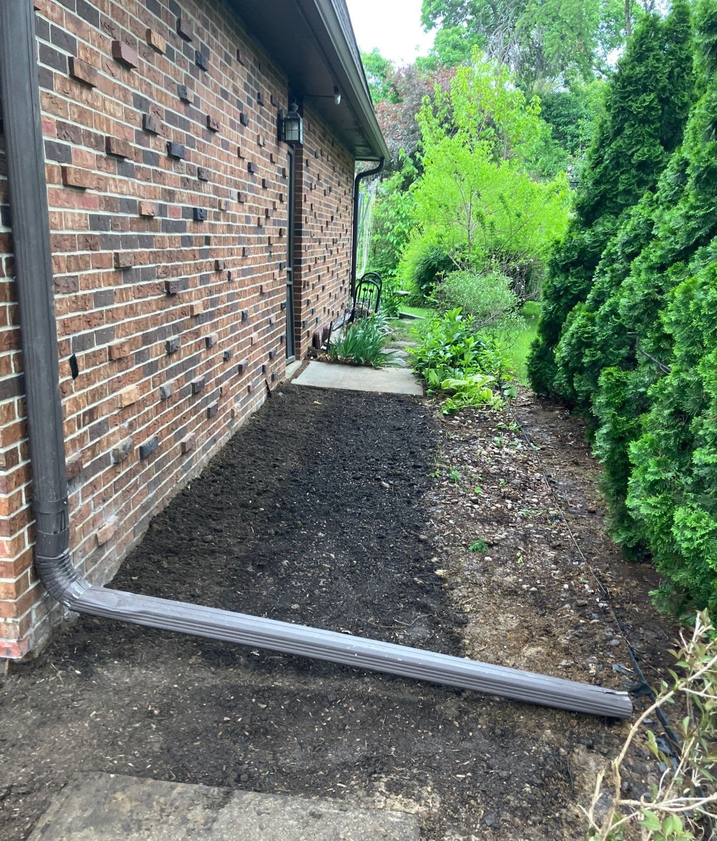 Epp Foundation Repair managing exterior drainage with a downspout and graded soil along a brick foundation.