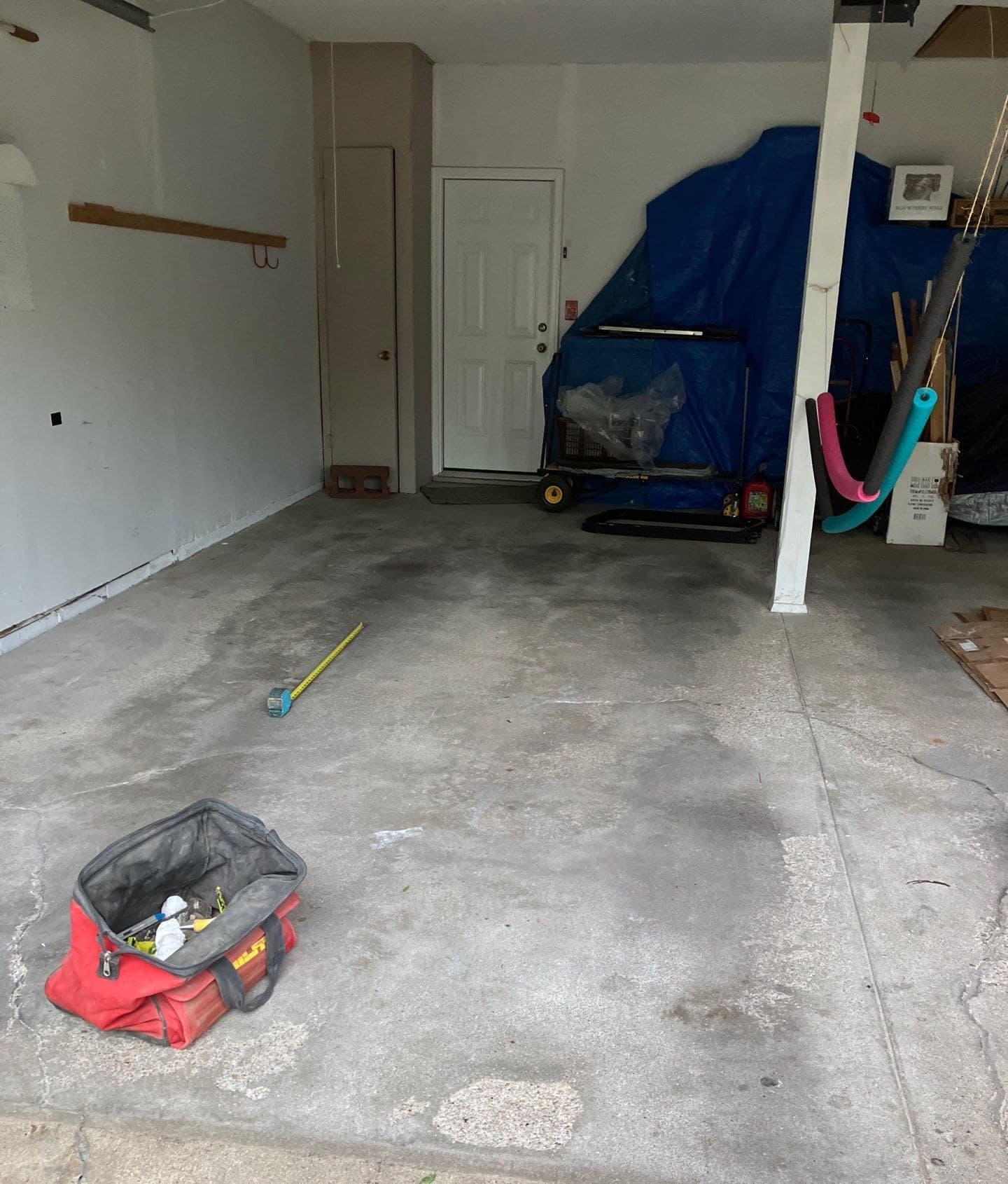 Epp Foundation Repair inspecting a cracked and stained concrete garage floor with a measuring tape and tool bag.