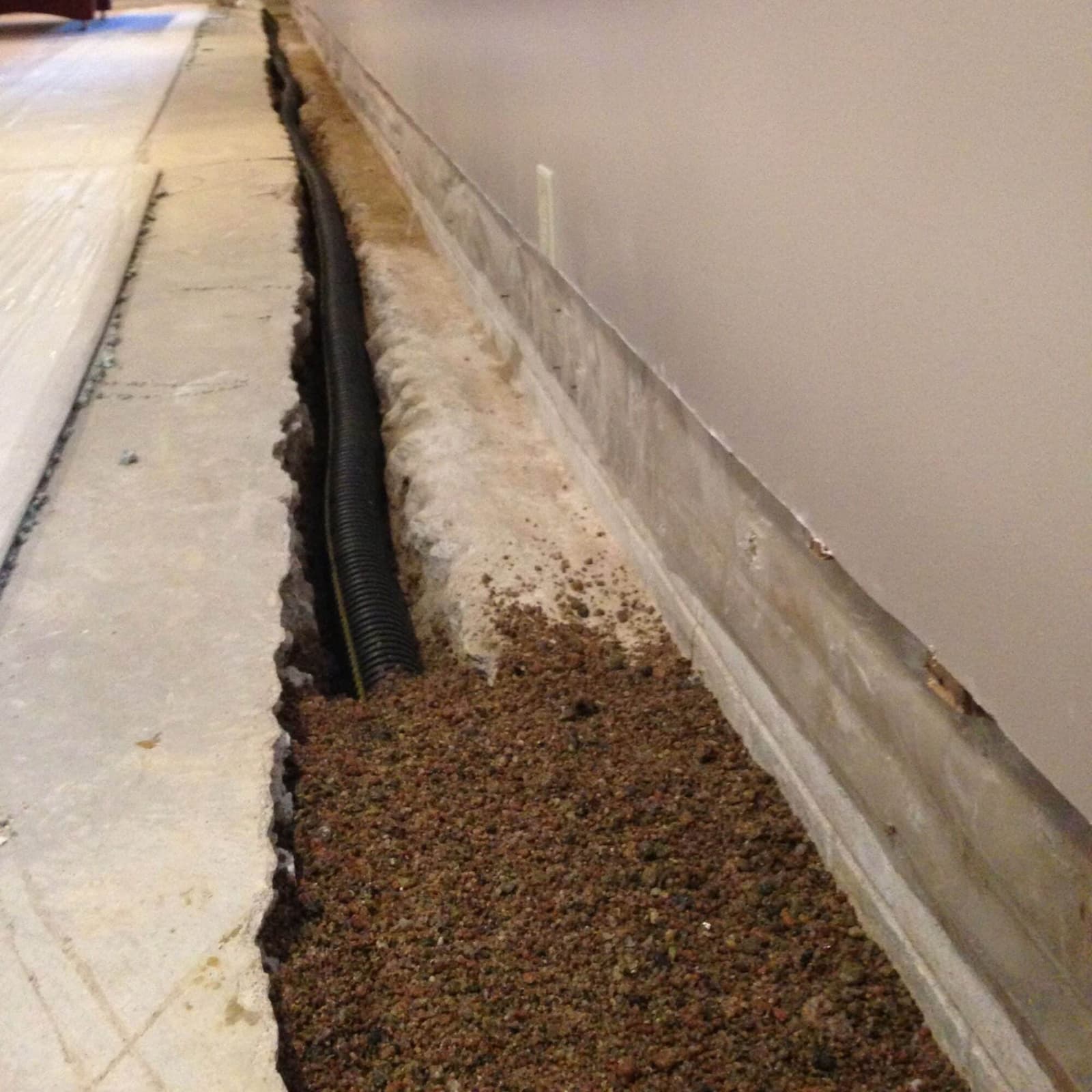 Epp Foundation Repair installing an interior French drain system with corrugated pipe and gravel in a basement.
