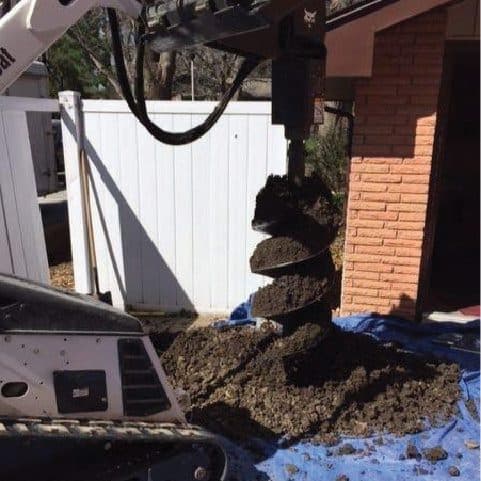 Epp Foundation Repair mini-excavator with an auger drilling a pilot hole for commercial helical piers.