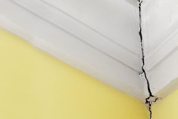 Epp Foundation Repair inspecting a diagonal crack where the wall meets the ceiling in an interior room.